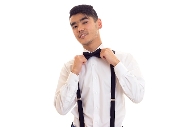 Elegant man in white shirt with black bow-tie and black suspenders on white background in studio
