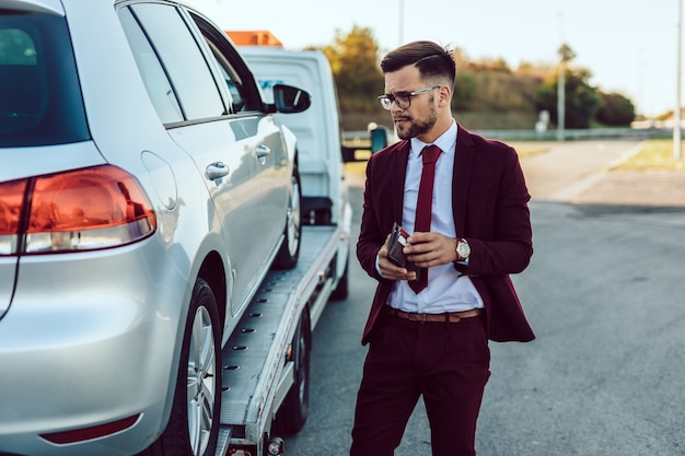 Elegant middle age business man calling towing service for help on the road. Roadside assistance concept.