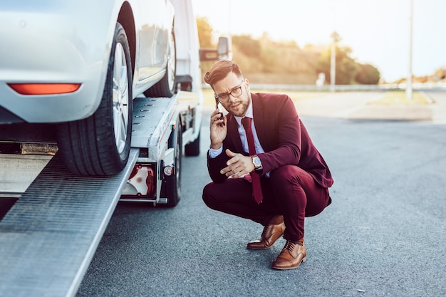 Elegant middle age business man calling towing service for help on the road. Roadside assistance concept.