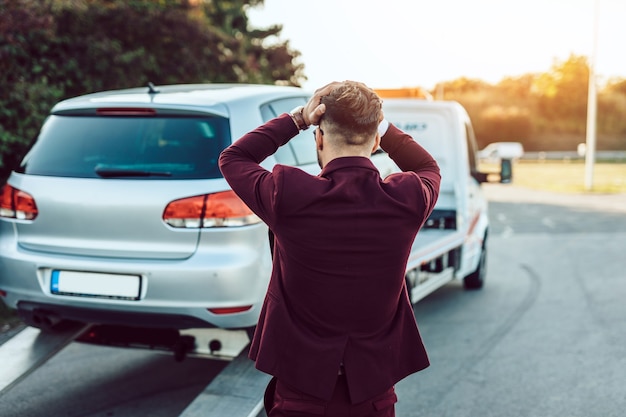 Elegante uomo d'affari di mezza età che utilizza il servizio di traino per aiutare l'incidente stradale sulla strada. concetto di assistenza stradale.