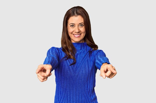 Elegant middleaged Caucasian woman in studio setting cheerful smiles pointing to front