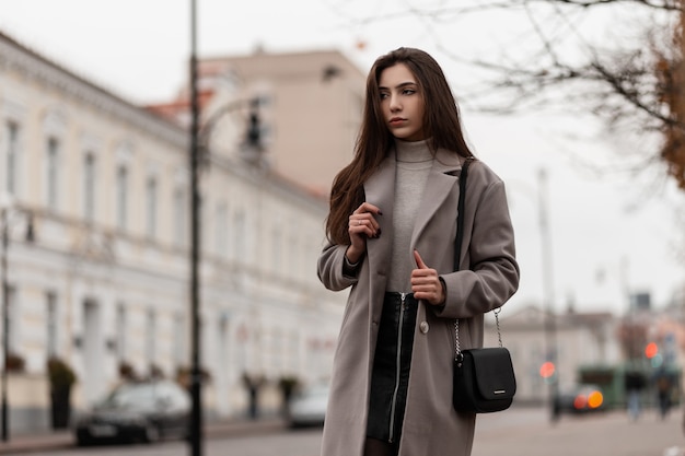 Elegant model with brown long hair in a stylish coat posing in the city on an autumn day