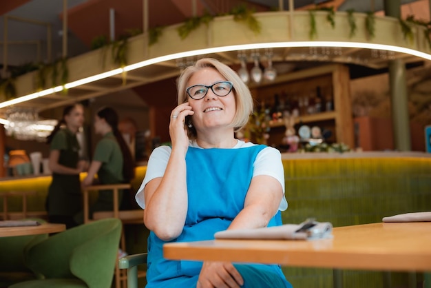 Elegant modern older mature senior woman with glasses is sitting in a cafe with a mobile phone with
