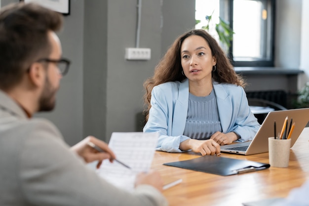 Elegant pretty financier talking to colleague with paper