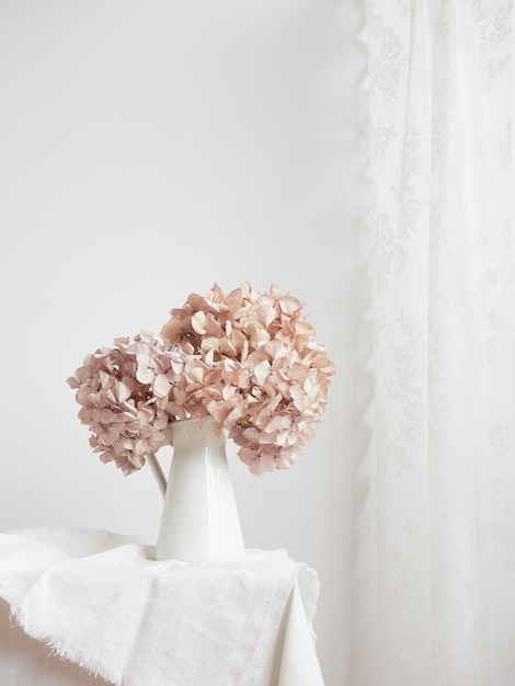 Elegant and simple composition of dried pink hydrangea flowers in a white vase on a white table with