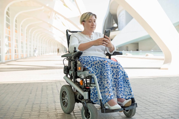 An elegant and smiling disabled woman sitting in a wheelchair uses the application on her mobile phone to explore the city