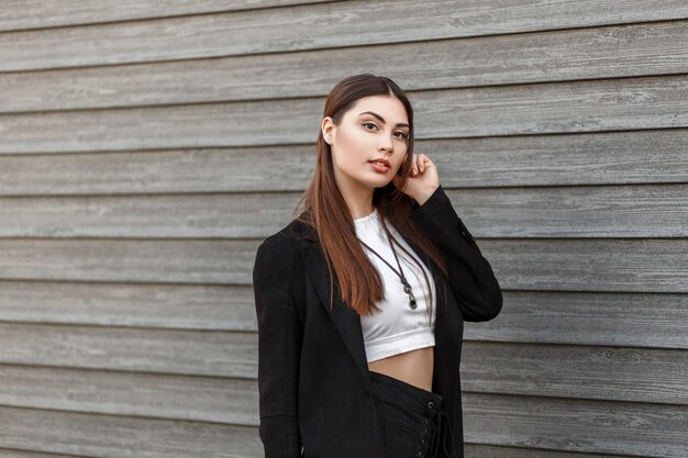 Elegant street fashion. Beautiful young woman in a black coat near a wooden wall