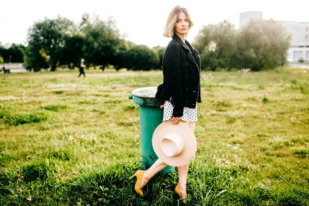 Elegant stylish blonde short hair girl posing with hat in the field