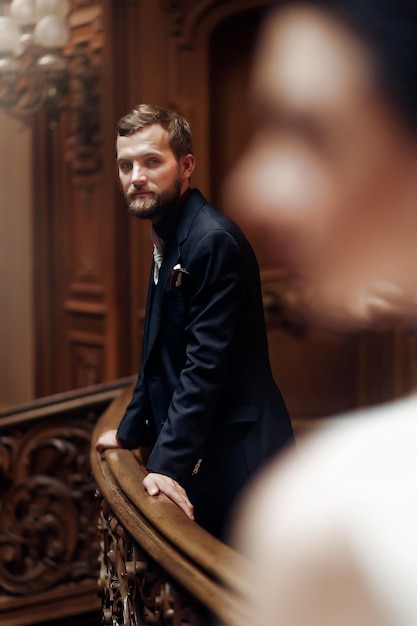 Elegant stylish handsome groom looking at gorgeous bride standing on wooden stairs in amazing old rich room unusual luxury wedding couple in retro stylexA