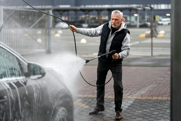 セルフサービスの洗濯ステーションで水鉄砲で車を掃除するエレガントでスタイリッシュな年配の男性