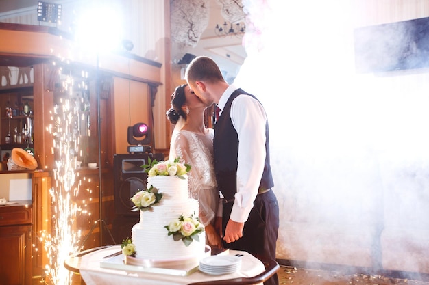 Elegant and stylish wedding cake with flowers Newlyweds standing near a large wedding cake