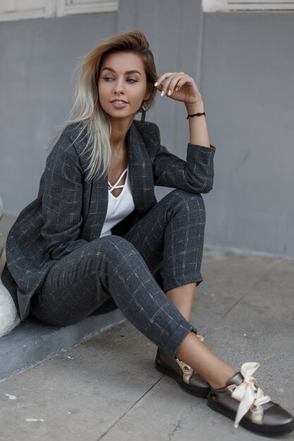 사진 거리에서 회색 벽 근처에 앉아 빈티지 회색 양복에 우아한 세련 된 젊은 여자. 패션