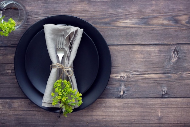 Elegant table setting with black plate silver cutlery glass of water and linen napkin on the wooden table Dining setting