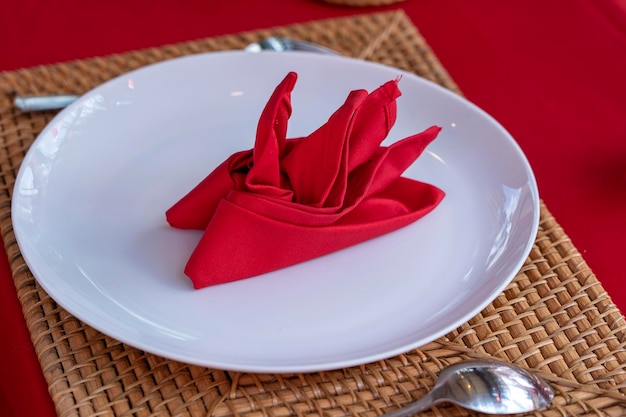 フォークスプーンの白いプレートとレストランの赤いナプキンを備えたエレガントなテーブルセッティングは、銀器とナプキンを配置した素敵なダイニングテーブルセットをクローズアップします