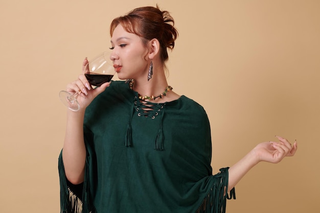Photo elegant transgender woman in teal poncho drinking glass of wine
