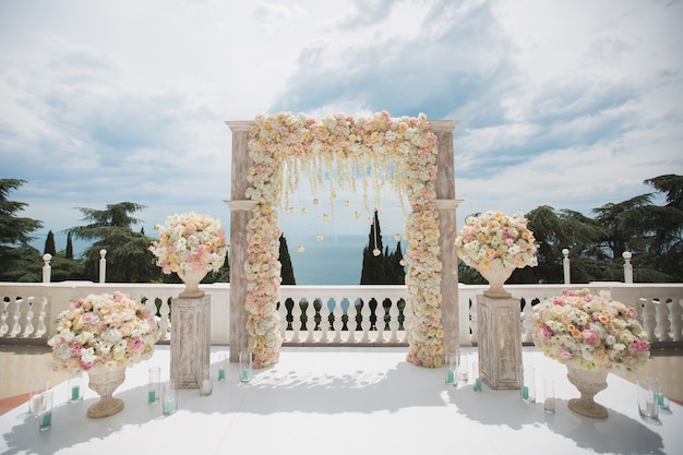 Elegante arco di nozze con fiori freschi, vasi sullo sfondo dell'oceano e del cielo blu.