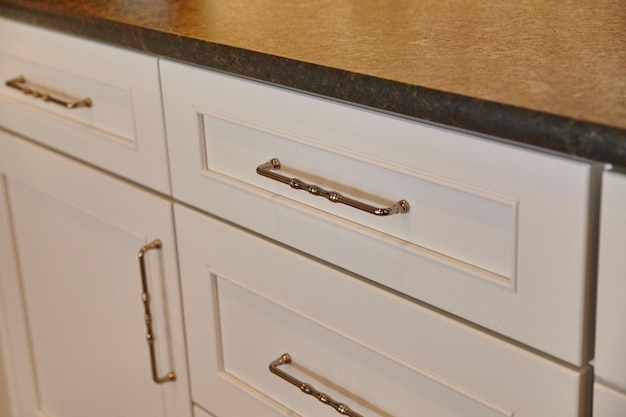 Photo elegant white cabinets with brass handles and granite countertop closeup view