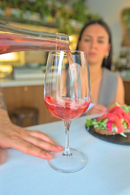 Elegant wine service waiter's hand pouring ros wine into a glass for woman seated at the bar blu