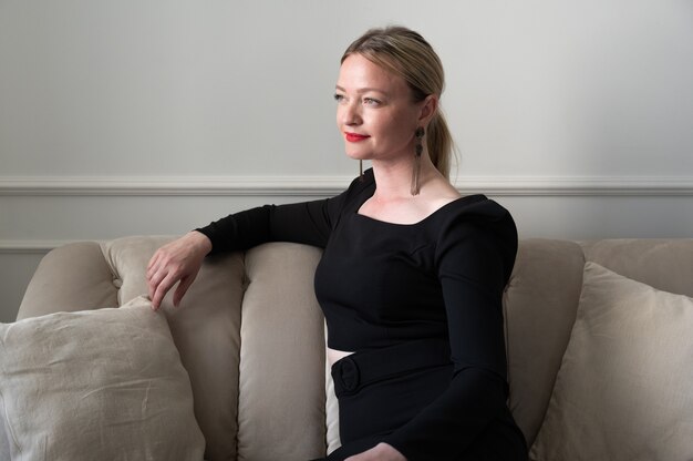 Elegant woman in black dress sits on the sofa.