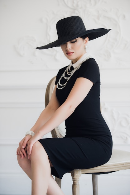 Donna elegante in abito nero con un cappello seduto sulla sedia