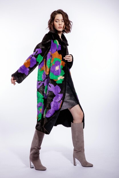 Elegant woman in black fur coat with colorful patterns suede boots posing on white background