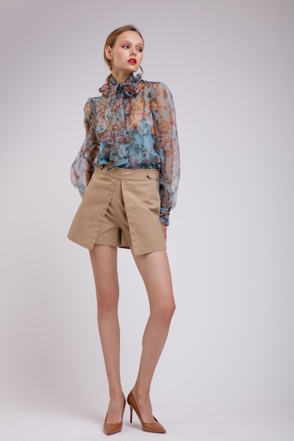 Elegant woman in blue blouse with  floral pattern  bow on the neck beige shorts on white background