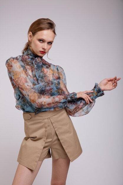 Elegant woman in blue blouse with  floral pattern  bow on the neck beige shorts on white background