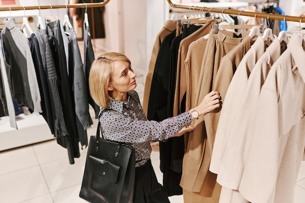 Elegant woman browsing clothes on racks in shopping mall