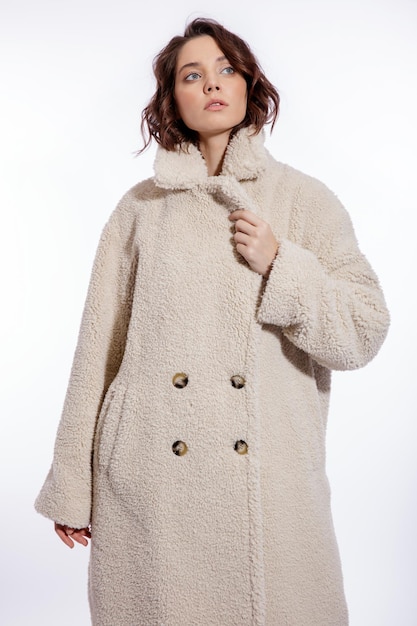 Elegant woman in cream beige fur coat  boots posing over white background Make up  Slim figure