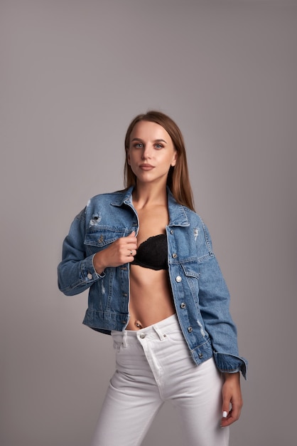 Photo elegant woman in denim jacket and white jeans posing on gray background