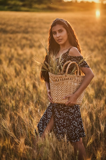 日没時の麦畑でバスケットとドレスのエレガントな女性。