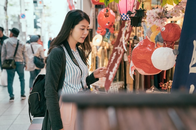 Photo elegant woman enjoy the beauty of the lantern shop. young traveler choosing souvenir in cute decoration vendor in market. girl having fun traveling outdoors during holidays in osaka.