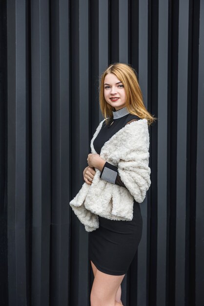 Elegant woman in little black dress and with fur scarf posing outside. Fashion concept