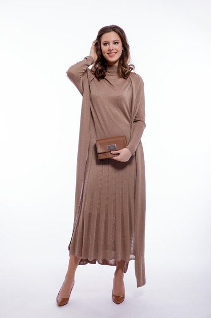 Elegant woman in long beige brown dress cardigan handbag clutch posing on white background