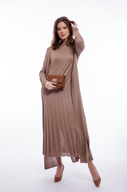 Elegant woman in long beige brown dress cardigan handbag clutch posing on white background