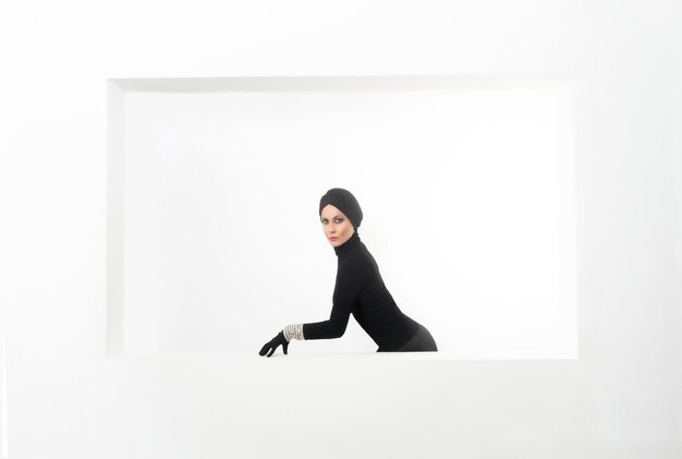 elegant woman made up and dressed in black with turban and gloves on a white background with copy sp