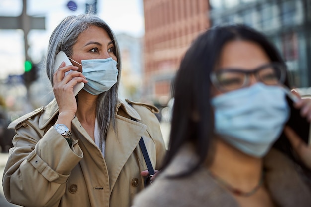 Foto donna elegante in maschera medica che ha conversazione telefonica all'aperto