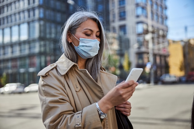 Photo elegant woman in medical mask using cellphone on the street