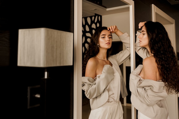 Elegant woman posing near mirror and looking at her reflection