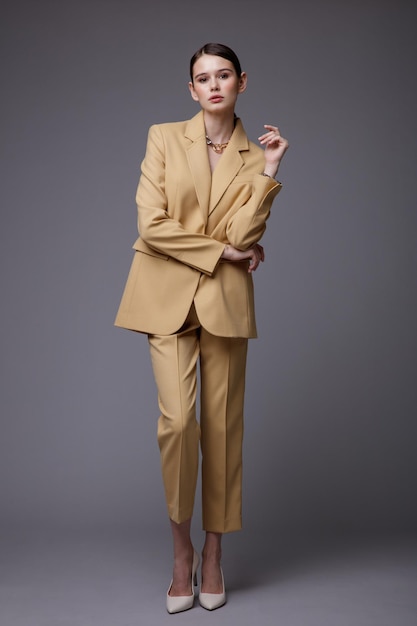 Elegant woman in pretty  beige sand suit jacket pants trousers accessories  on gray background