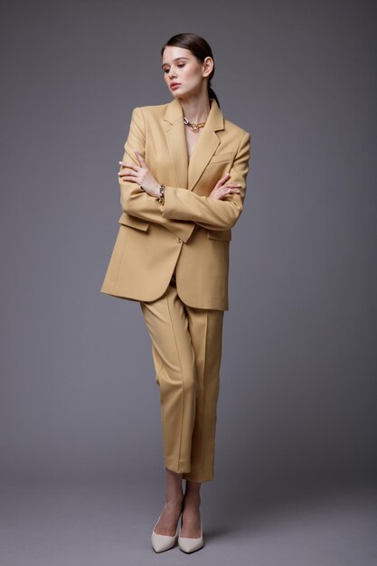 Elegant woman in pretty  beige sand suit jacket pants trousers accessories  on gray background