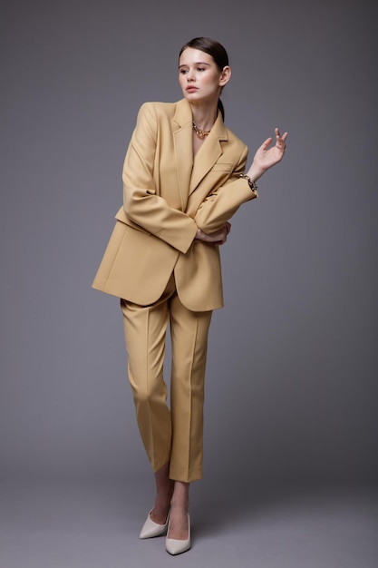 Elegant woman in pretty  beige sand suit jacket pants trousers accessories  on gray background