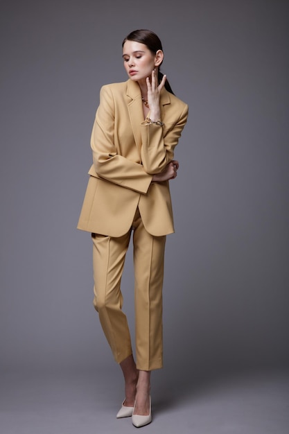 Elegant woman in pretty  beige sand suit jacket pants trousers accessories  on gray background