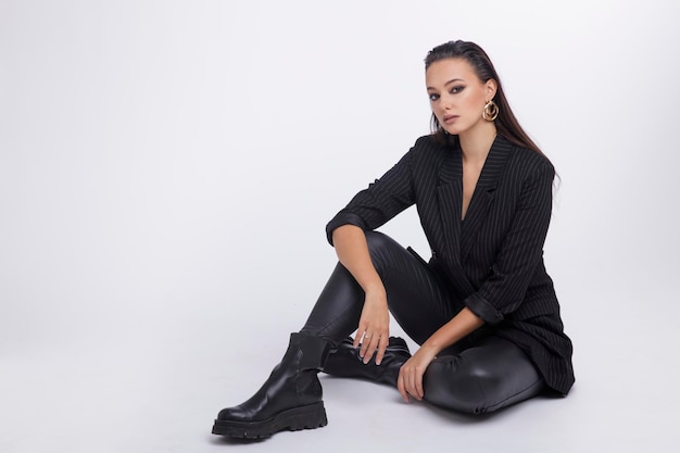 Elegant woman in pretty black jacket, leather pants, boots on\
white background.