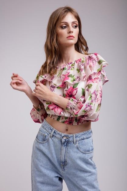 Elegant woman in pretty blouse top with floral pattern in red blue jeans on white background