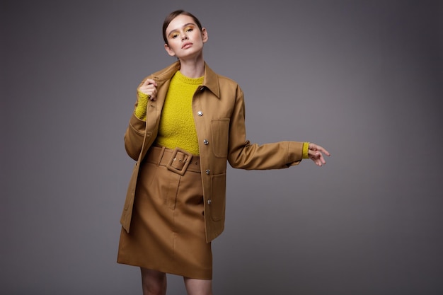 Elegant woman in a pretty brown beige sand jacket skirt yellow mustard sweater on gray background