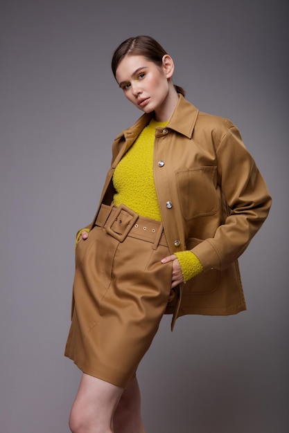 Elegant woman in a pretty brown beige sand jacket skirt yellow mustard sweater on gray background