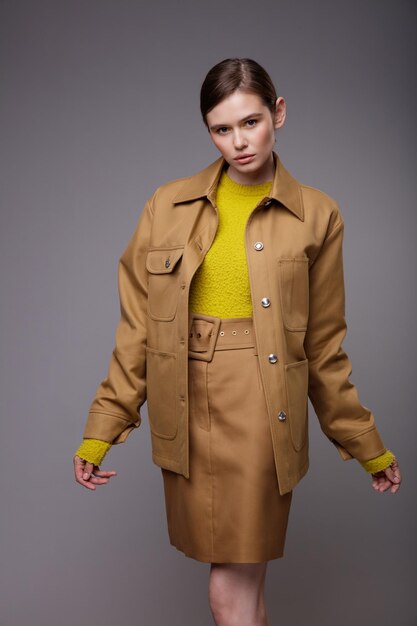 Elegant woman in a pretty brown beige sand jacket skirt yellow mustard sweater on gray background