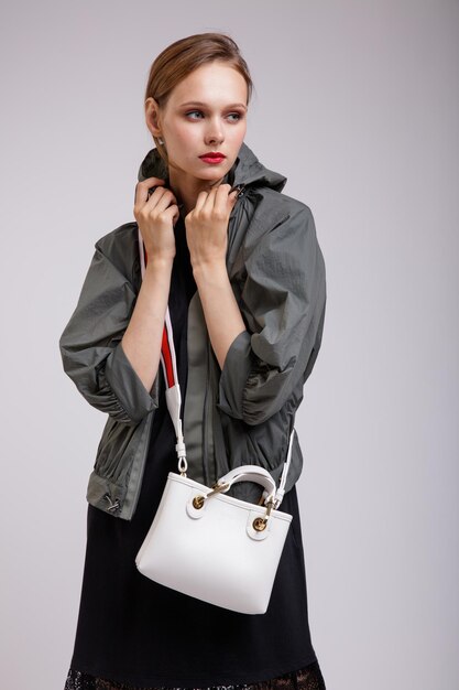 Elegant woman in pretty green jacket black skirt handbag with red strap posing on white background