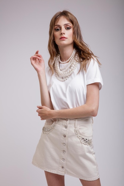 Elegant woman in pretty white denim skirt tshirt pearl necklace posing over soft gray background